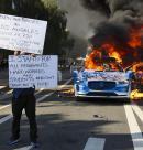LOS ANGELES (United States), 08/06/2025.- An activist holds signs as a car burns during protests sparked by immigration raids in Los Angeles, California, USA, 08 June 2025. US President Donald Trump has deployed 2,000 National Guard troops, despite not receiving a request from the state of California for any additional assistance, following large protests against ongoing immigration enforcement raids in the Los Angeles area over the last couple of days. (Protestas) EFE/EPA/ALLISON DINNER